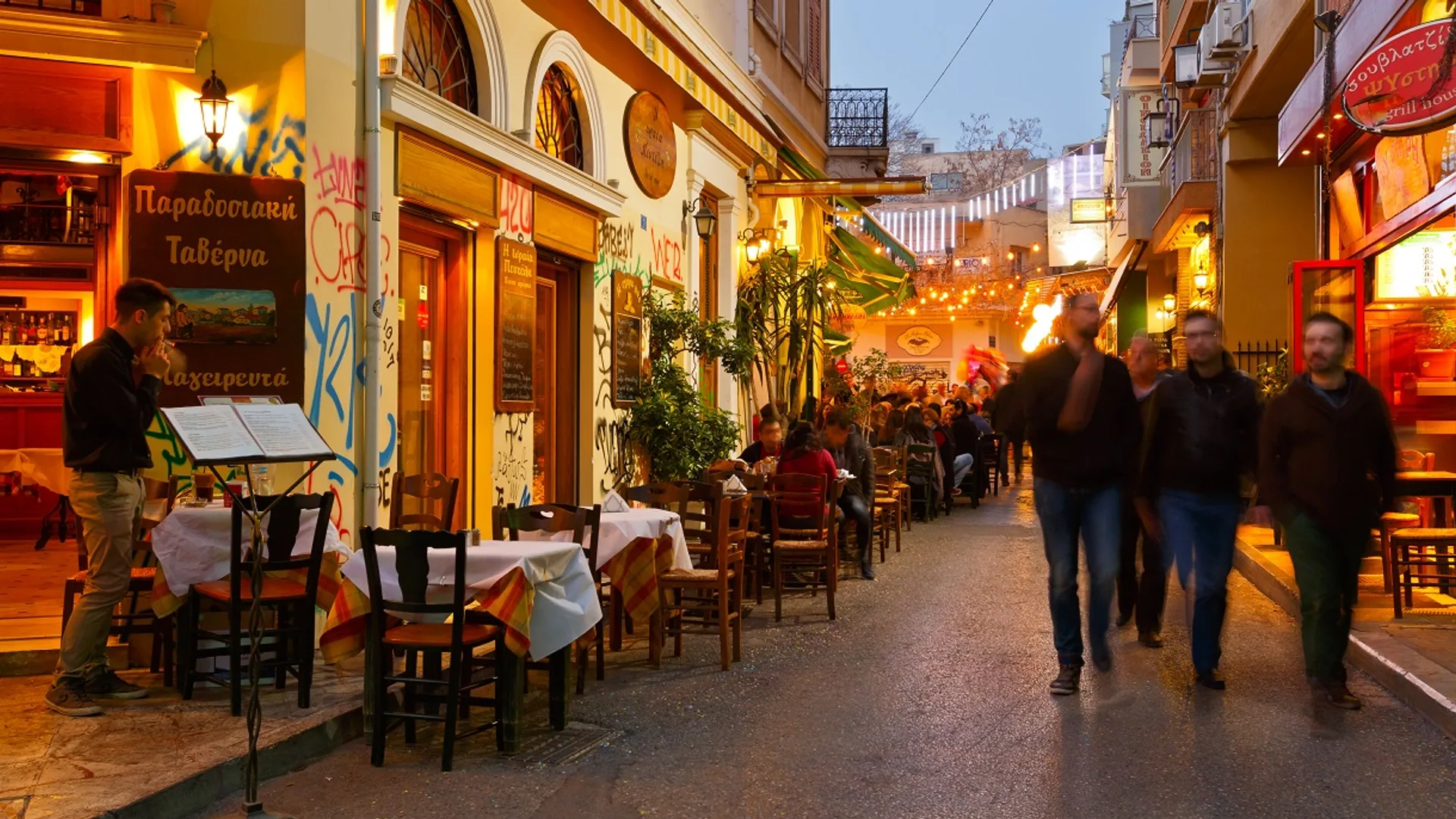 A colourful Psyrrí alley at night with a packed taverna and a bouzouki visible inside