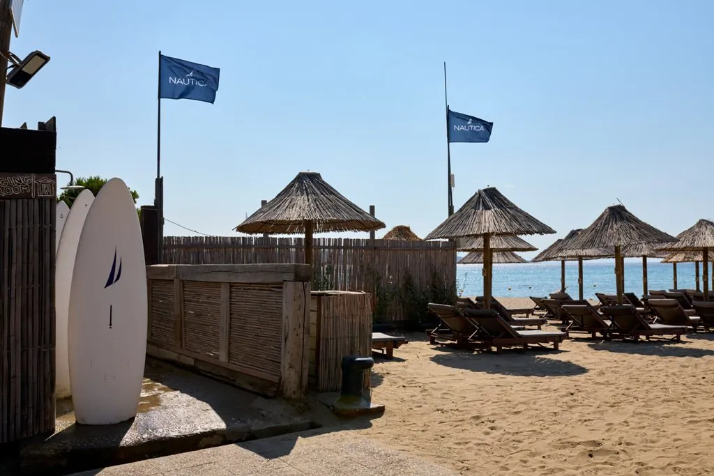 Der organisierte Abschnitt von Schinias mit Strohschirmen, Holzliegen, SUP-Boards und dem glitzernden Meer im Hintergrund