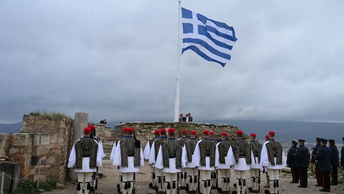 Οι εύζωνες της Προεδρικής Φρουράς παρατεταγμένοι κάτω από τη μεγάλη ελληνική σημαία στην Ακρόπολη, με μπάντα στα δεξιά