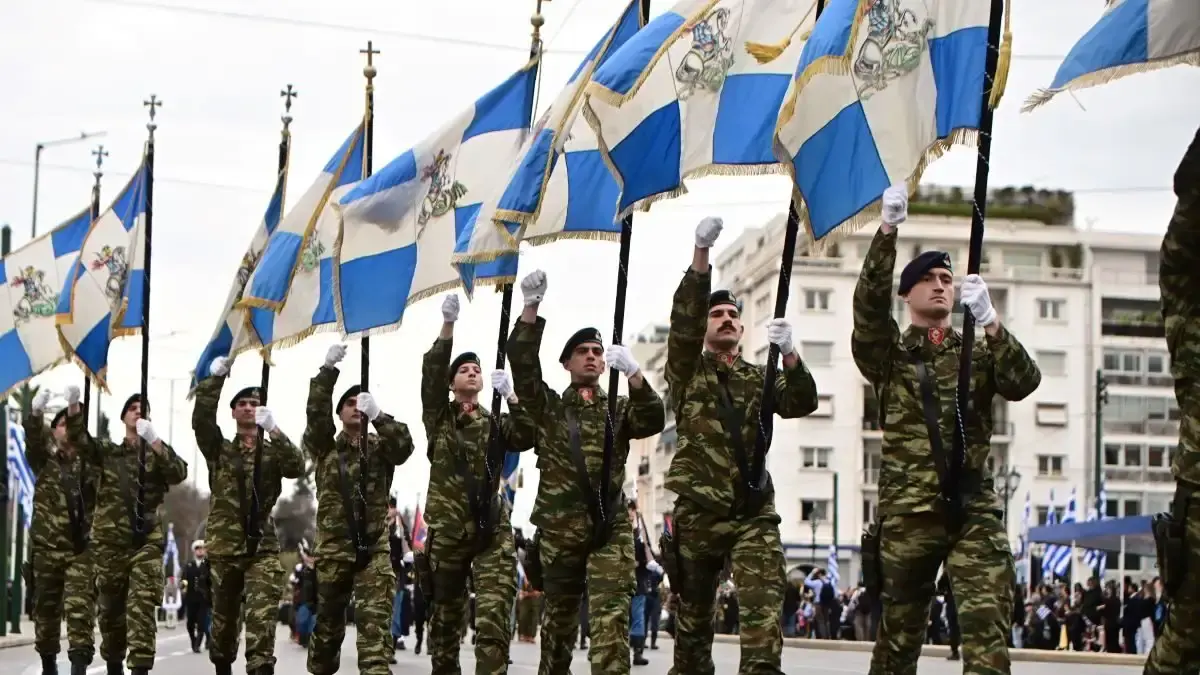 Σημαιοφόροι με γαλανόλευκες πολεμικές σημαίες και λευκά γάντια παρελαύνουν σε κεντρικό δρόμο της Αθήνας