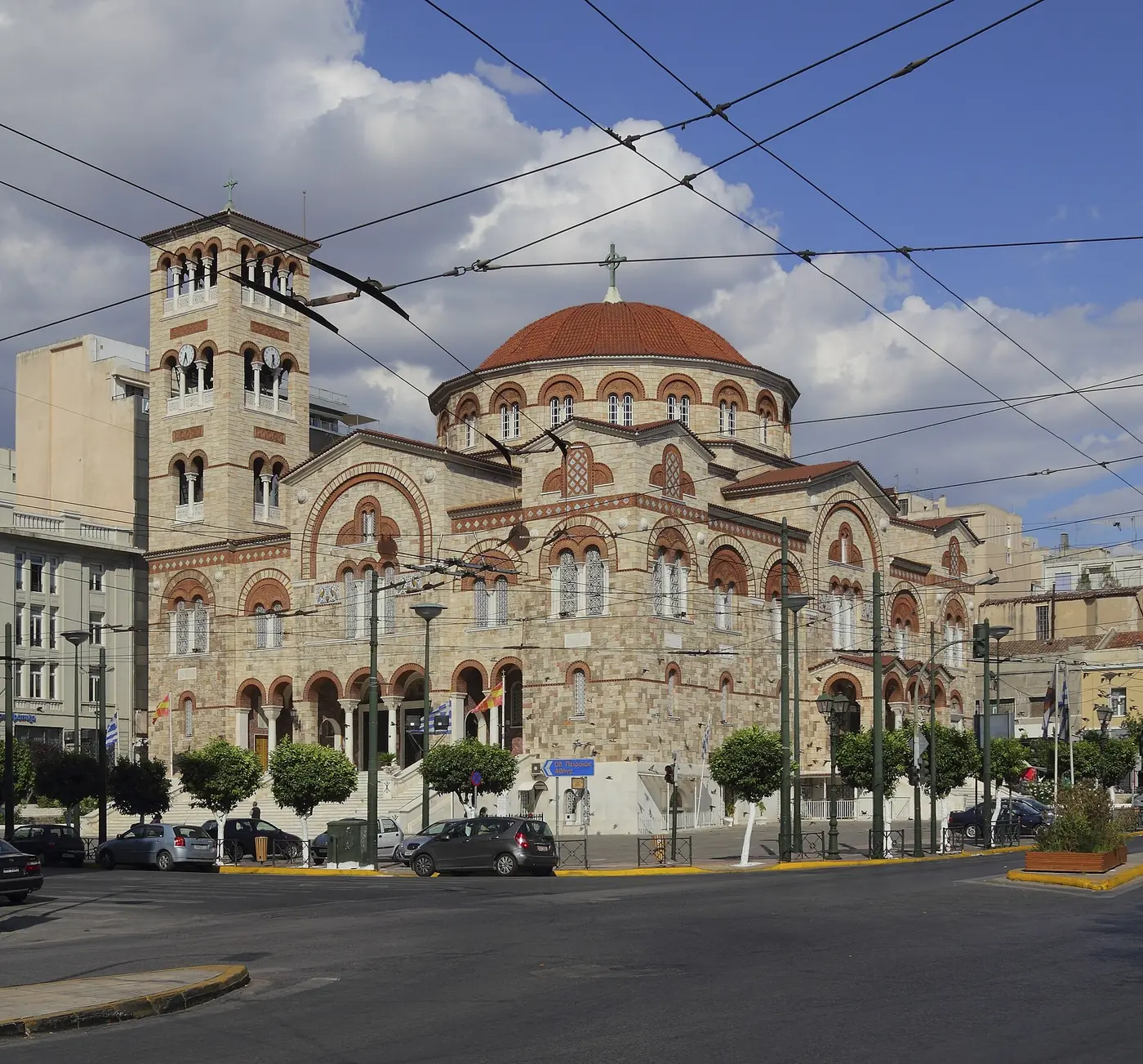 Агия Триада в Пирея от улицата, с жици на тролейбуса и паркирани коли отпред