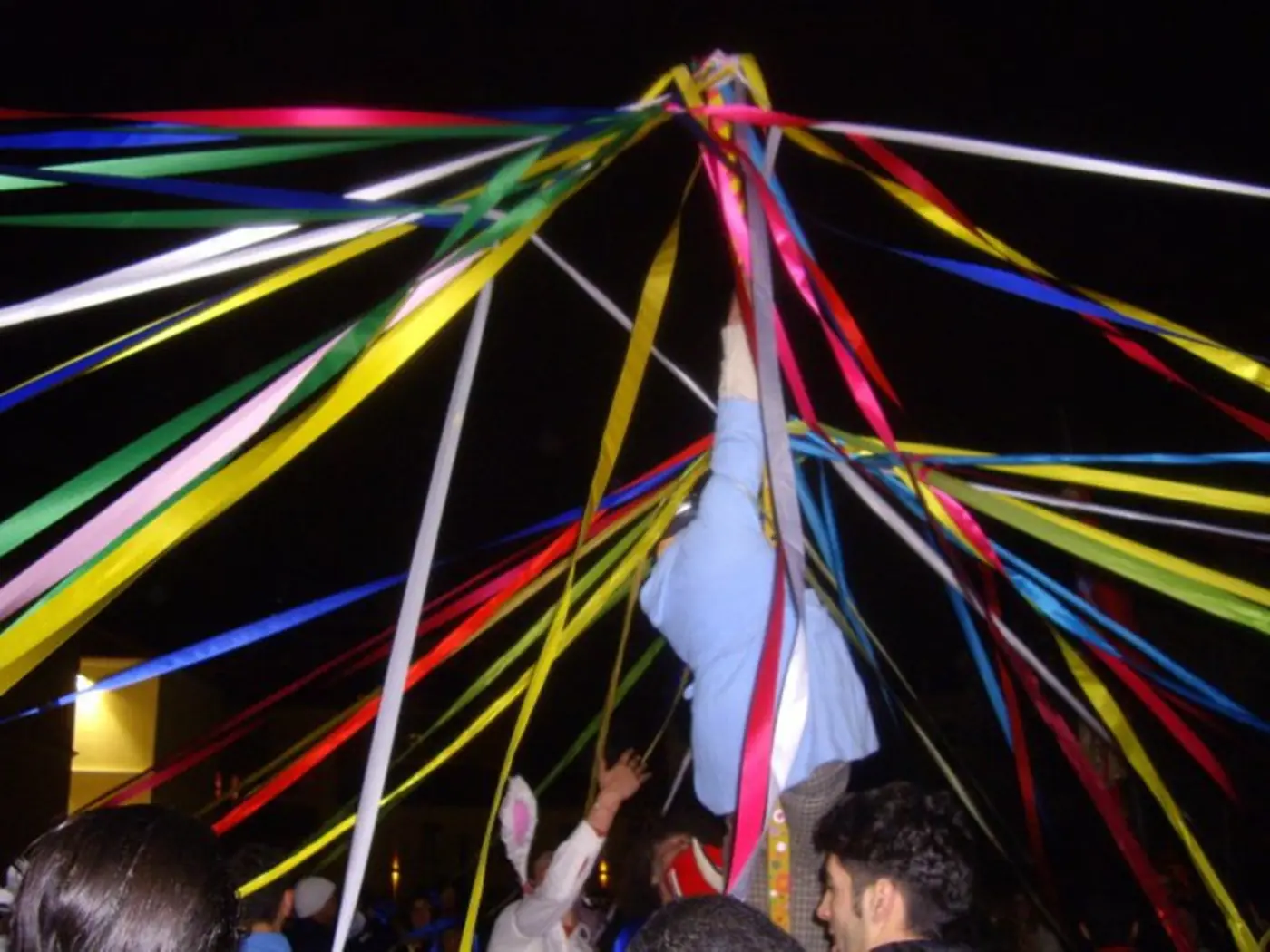 Rubans colorés du gaitanaki tendus vers le ciel nocturne, tenus par les mains des danseurs