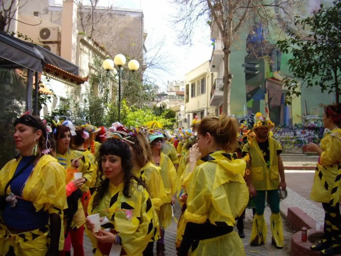 Des dizaines de carnavaliers en costumes jaunes et dorés marchent dans une rue de Metaxourgeio entre des maisons néoclassiques