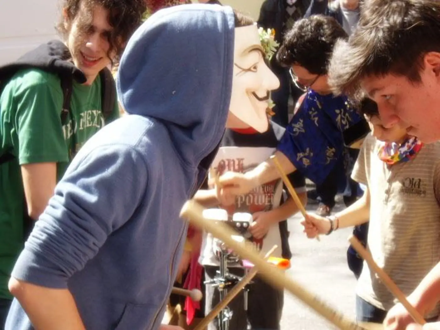 Jeunes en capuches et costumes rouges jouant des percussions en cercle au carnaval de Metaxourgeio