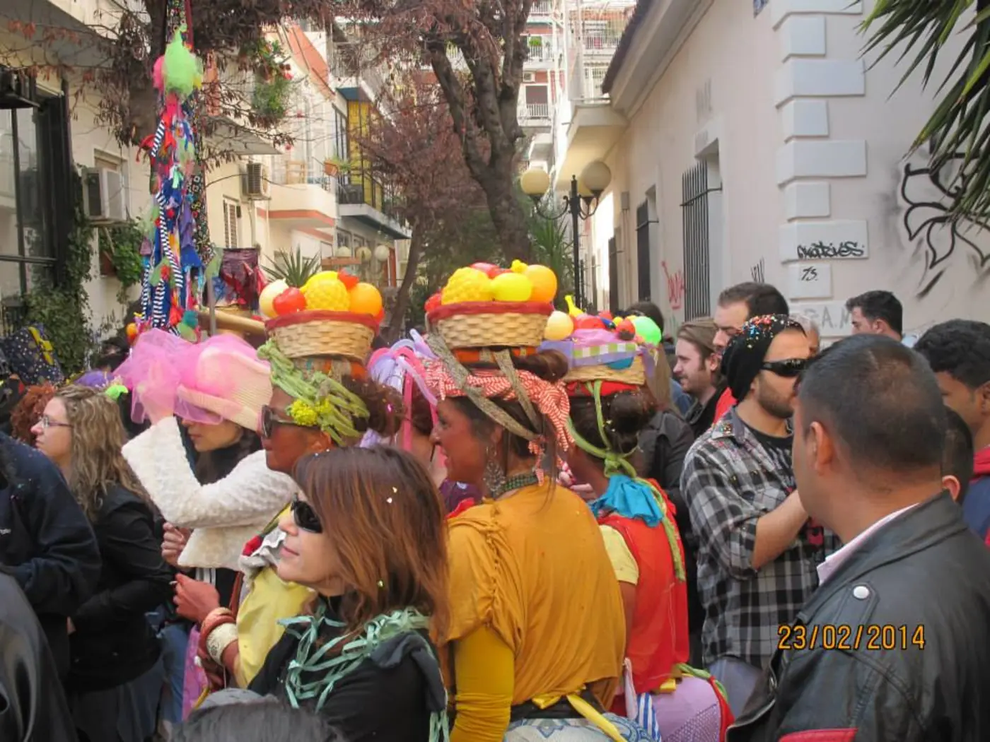 Personnes déguisées avec des chapeaux colorés parmi des spectateurs dans une rue étroite bordée d’arbres