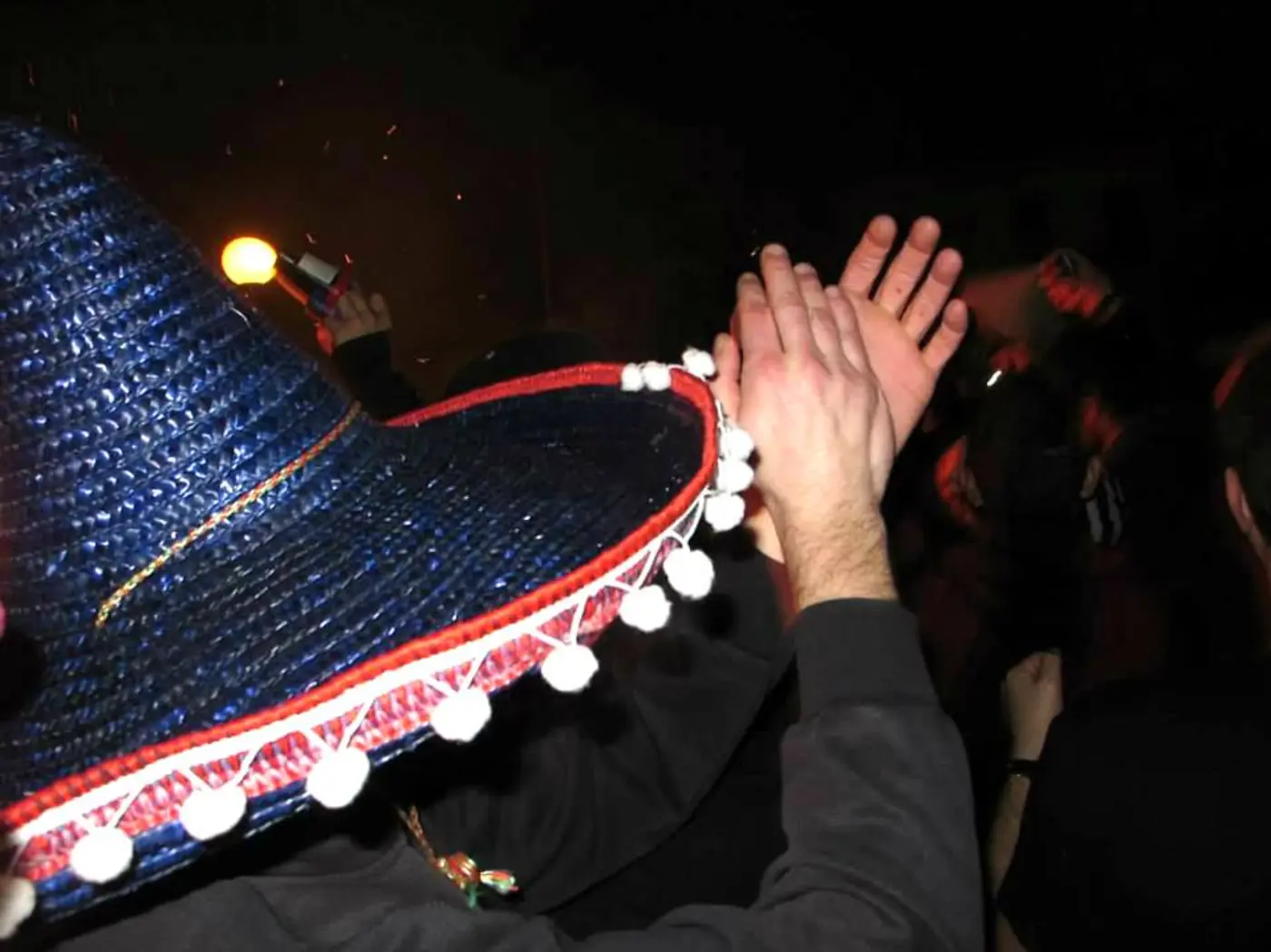 Sombrero bleu à pompons blancs au-dessus de mains qui applaudissent dans l’obscurité