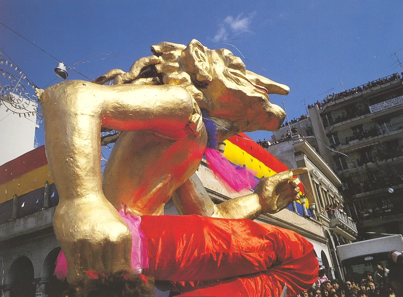 Char doré en forme de lion avec des tentures rouges et jaunes passant entre des immeubles de Patras