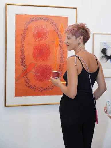 Une visiteuse, gobelet à la main, regarde un tableau orange dans un cadre doré