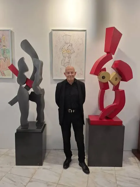 Deux sculptures abstraites en métal, une grise et une rouge, sur des socles noirs, avec un homme entre les deux