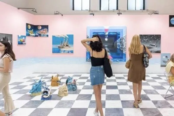 Visiteuses dans une salle rose avec des tableaux aux murs et de petites sculptures en céramique sur un sol en damier noir et blanc