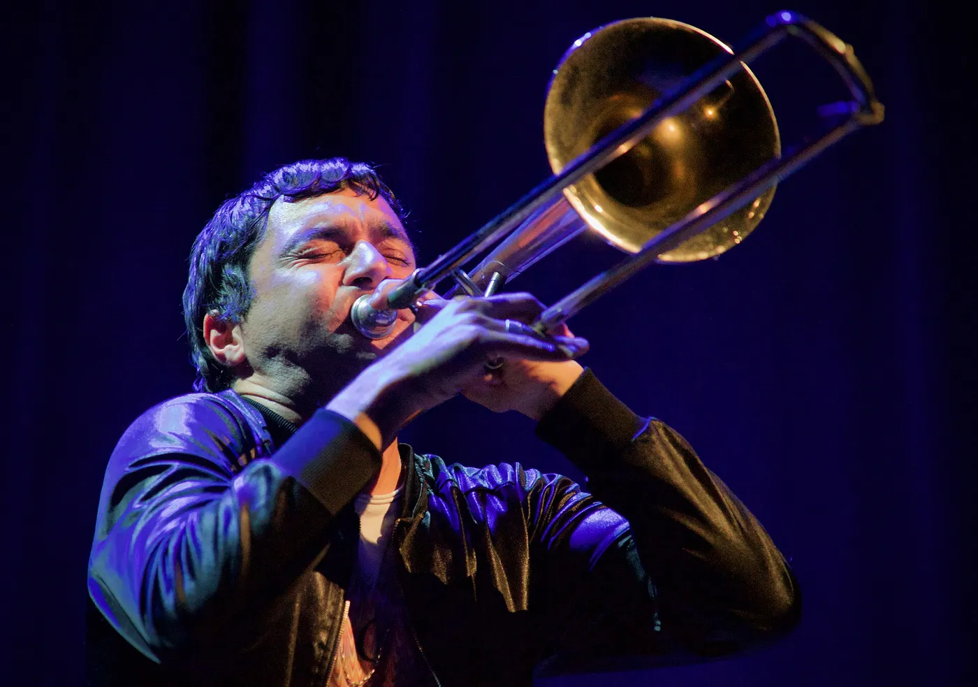 Gianluca Petrella spielt Posaune mit geschlossenen Augen, in blauem Licht