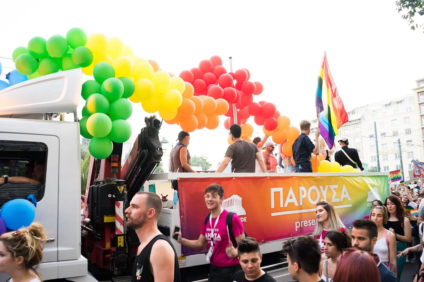 Платформа със зелена, жълта и червена арка от балони и млади хора, които танцуват пред нея на улицата