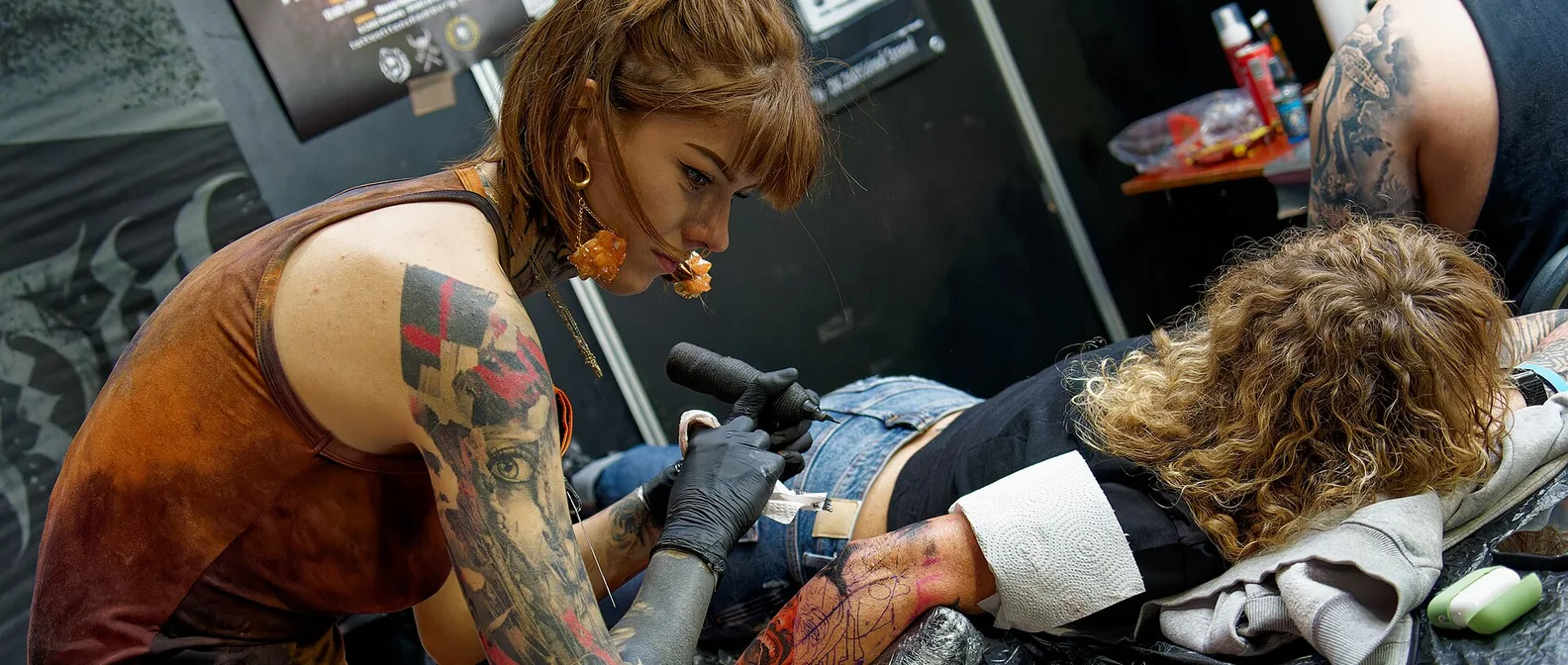 Un tatuatore con le braccia tatuate lavora su un cliente in uno stand della convention