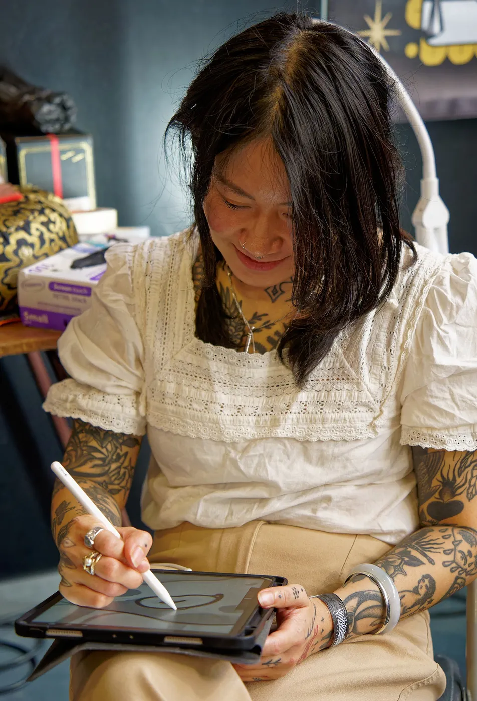 Una tatuatrice disegna su un tablet, con le braccia tatuate