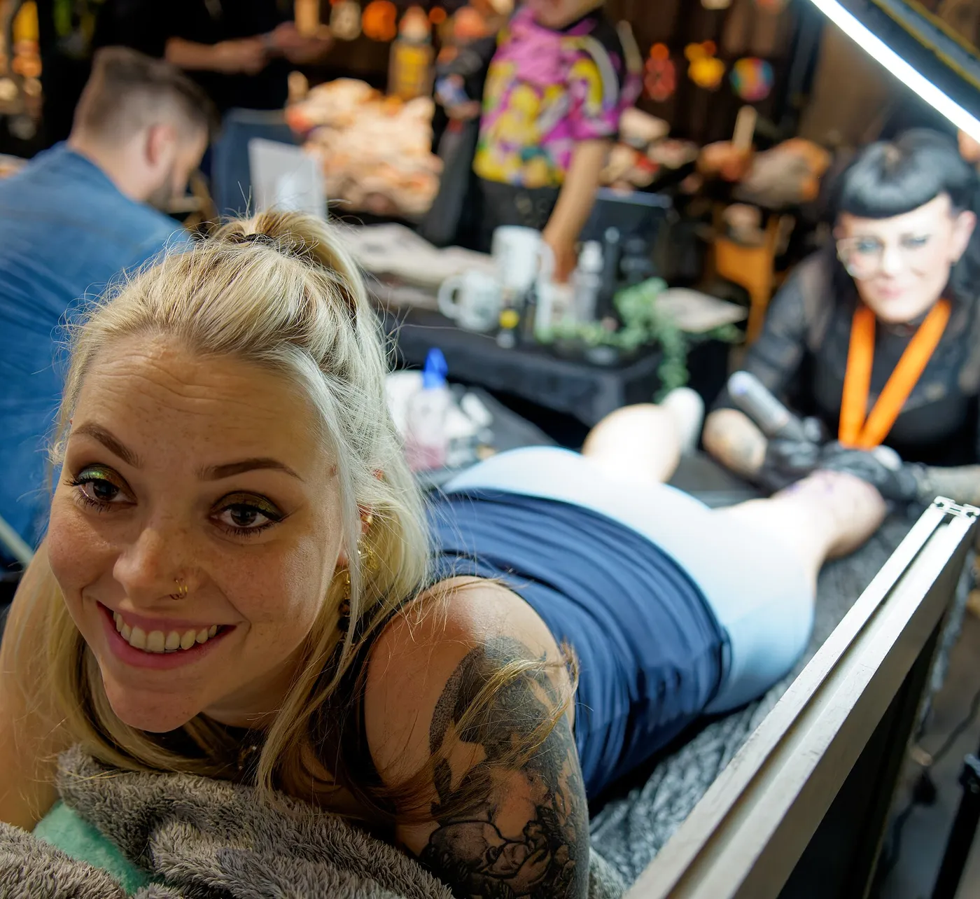 Una donna sorridente sdraiata su un lettino mentre la tatuano a una convention