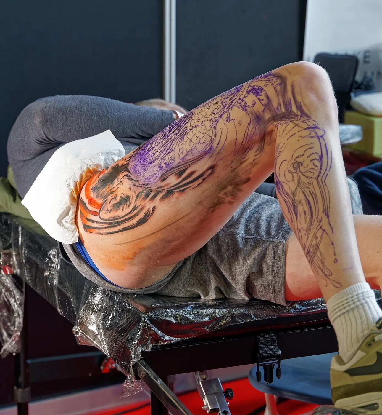 Una ragazza seduta in uno stand mentre un tatuatore le tatua il braccio