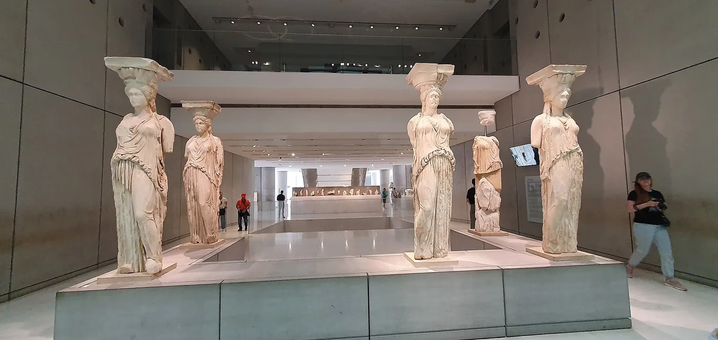 As Cariátides originais em fila dentro do Museu da Acrópole, com visitantes à volta