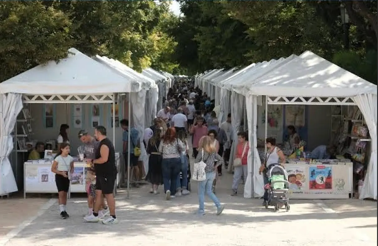 Λευκά περίπτερα εκδοτών κάτω από τα δέντρα του Πεδίου του Άρεως με κόσμο να περπατά ανάμεσά τους τη μέρα