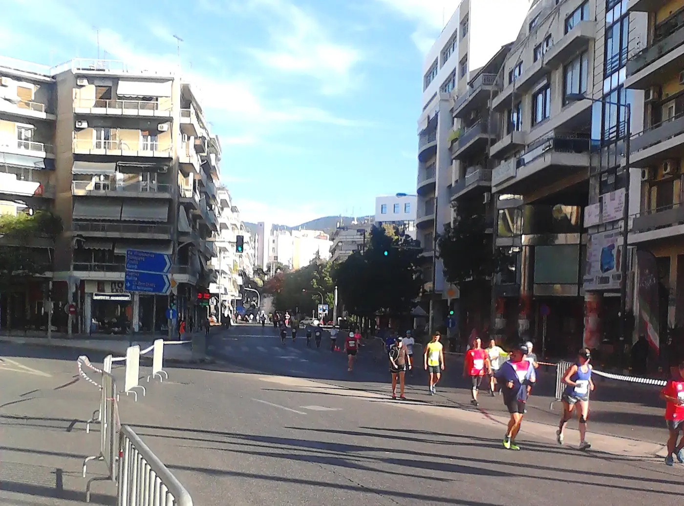 Δρομείς σε άδειο δρόμο της Αθήνας, με κάγκελα στο πεζοδρόμιο και πολυκατοικίες στις δύο πλευρές