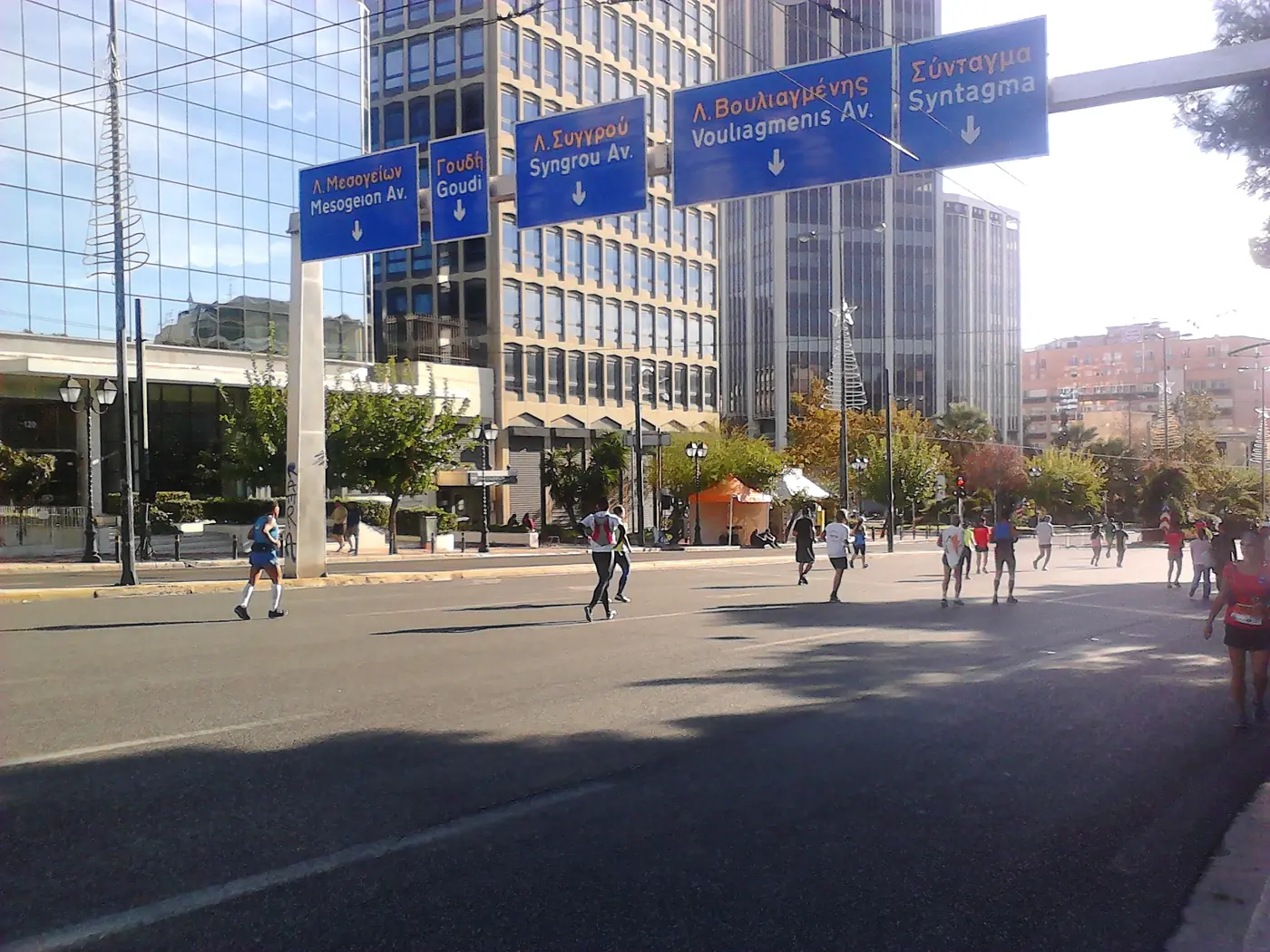 Δρομείς κάτω από μπλε πινακίδες για Μεσογείων και Συγγρού, ανάμεσα σε κτίρια γραφείων
