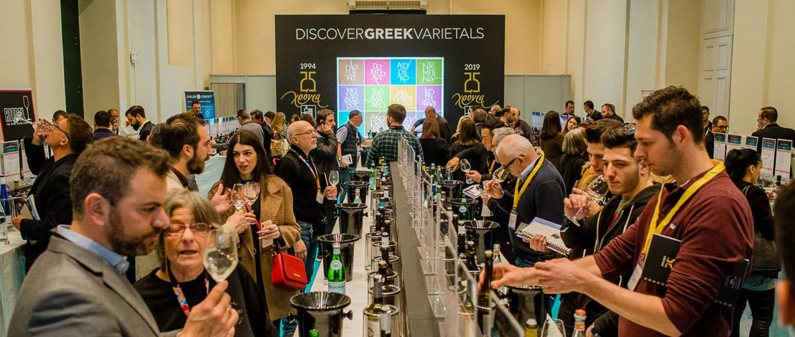 Des visiteurs dégustent des vins à un long comptoir de dégustation à l’Oenorama, sous une bannière pour les 25 ans du salon