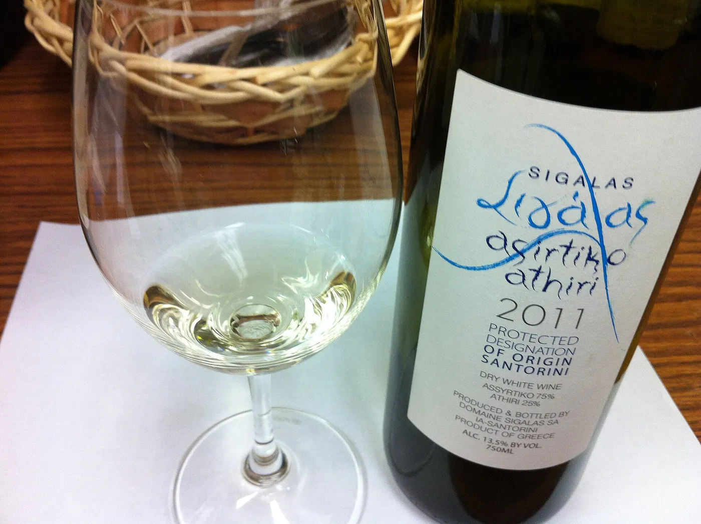 Un verre de vin blanc à côté d’une bouteille d’assyrtiko athiri de Santorin