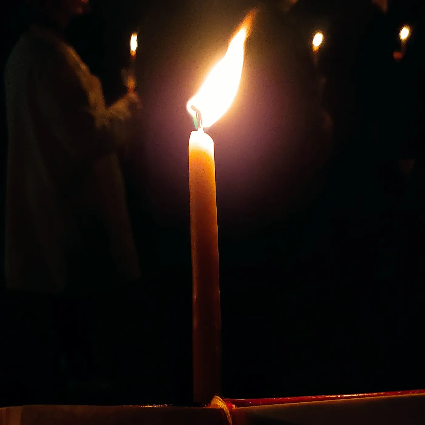 Un cierge de Pâques allumé dans une église sombre la nuit de la Résurrection, avec la flamme de la Sainte Lumière
