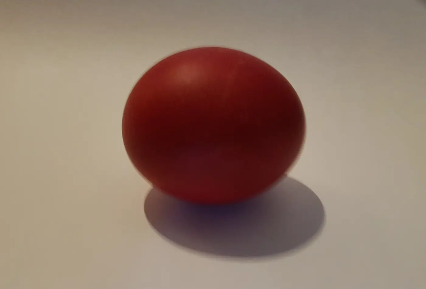 Un œuf de Pâques teint en rouge sur une surface blanche avec son ombre