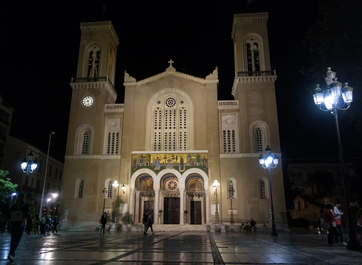 La façade de la Métropole d’Athènes illuminée la nuit, avec ses deux clochers et les lampadaires de la place