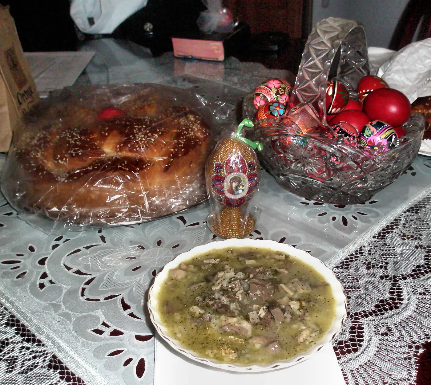 Table de Pâques avec tsoureki, un bol d’œufs rouges, une assiette de magiritsa et un cierge de Pâques sur une nappe brodée