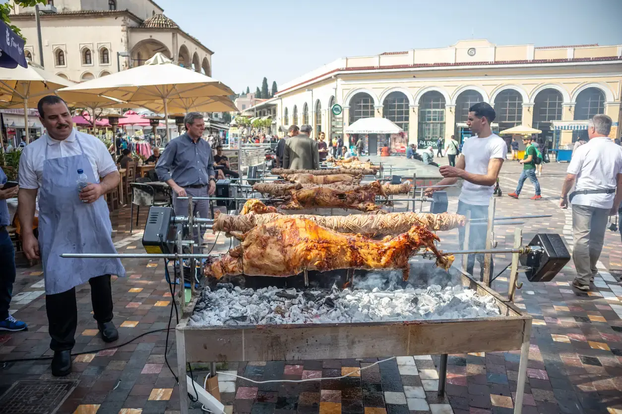 Des agneaux et des kokoretsi tournent à la broche sur la braise place Monastiraki, avec l’ancienne mosquée et la station de métro derrière
