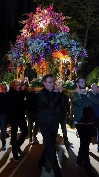Des hommes portent sur leurs épaules l’Épitaphe décoré de fleurs violettes et blanches dans une allée du parc la nuit