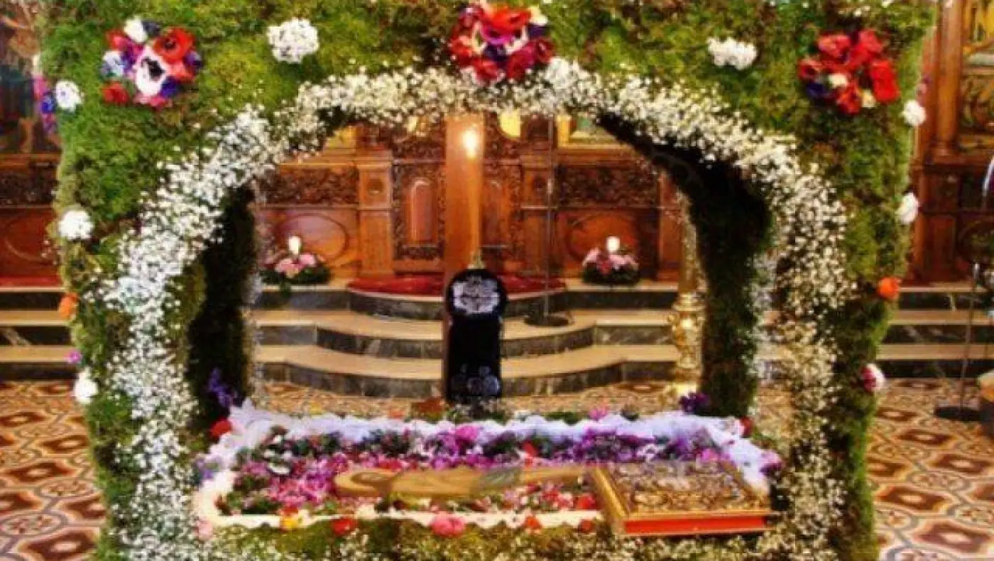 L’Épitaphe dans l’église, sous une arche de branches vertes, de fleurs blanches et d’anémones rouges, devant l’iconostase en bois sculpté