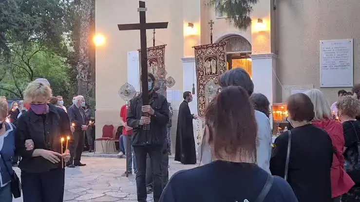 Des fidèles aux cierges allumés, la croix et les éventails liturgiques devant l’église des Taxiarques au Pedion tou Areos au crépuscule