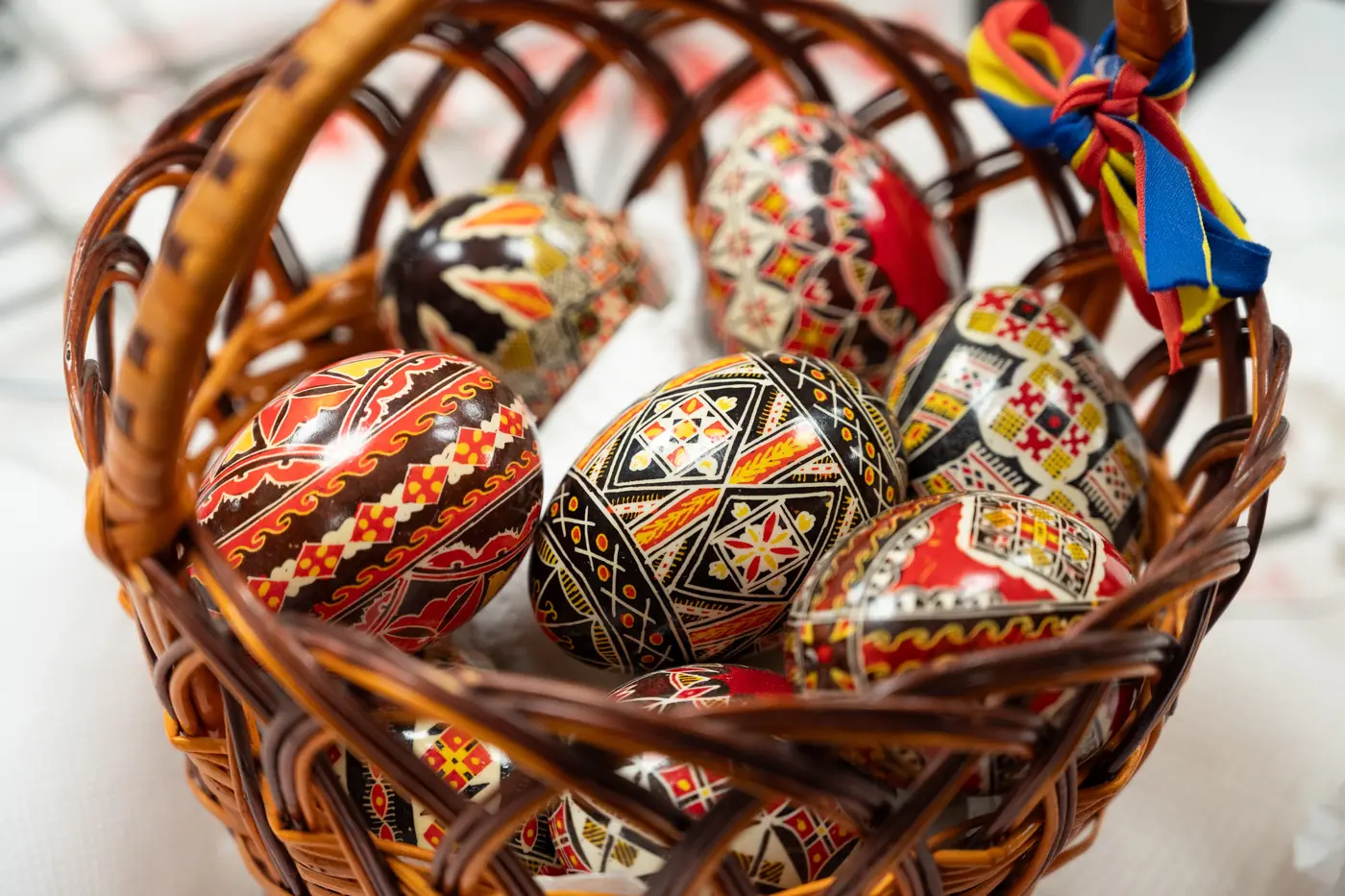 Un panier en paille plein d’œufs de Pâques peints de motifs géométriques rouges, noirs et jaunes, avec un ruban coloré