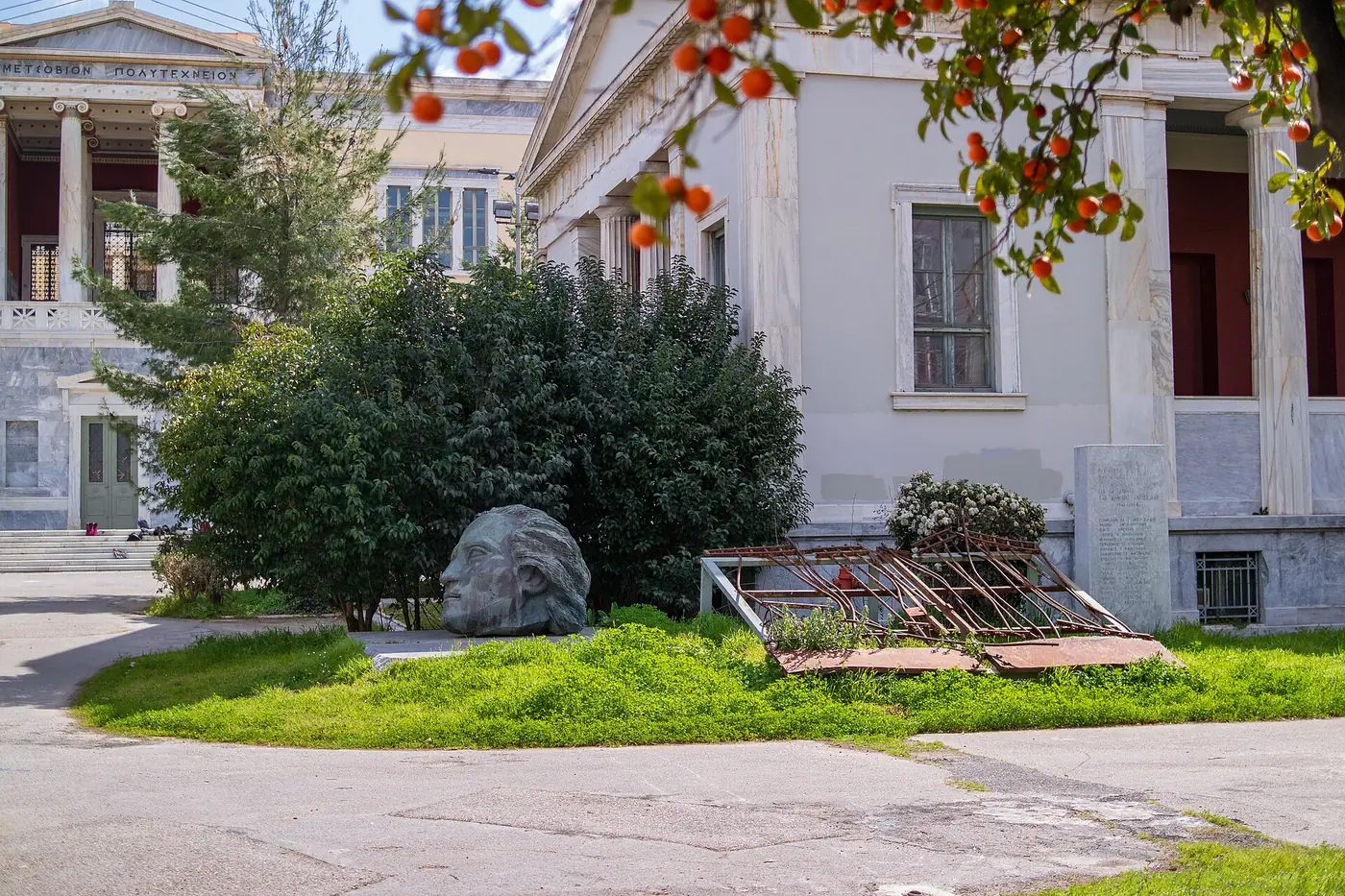 Il memoriale nel cortile del Politecnico, tra cespugli ed edifici neoclassici, con un arancio amaro davanti