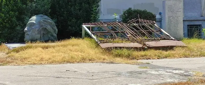 Il cancello di ferro spezzato del Politecnico da vicino, steso sull’erba con le sbarre piegate