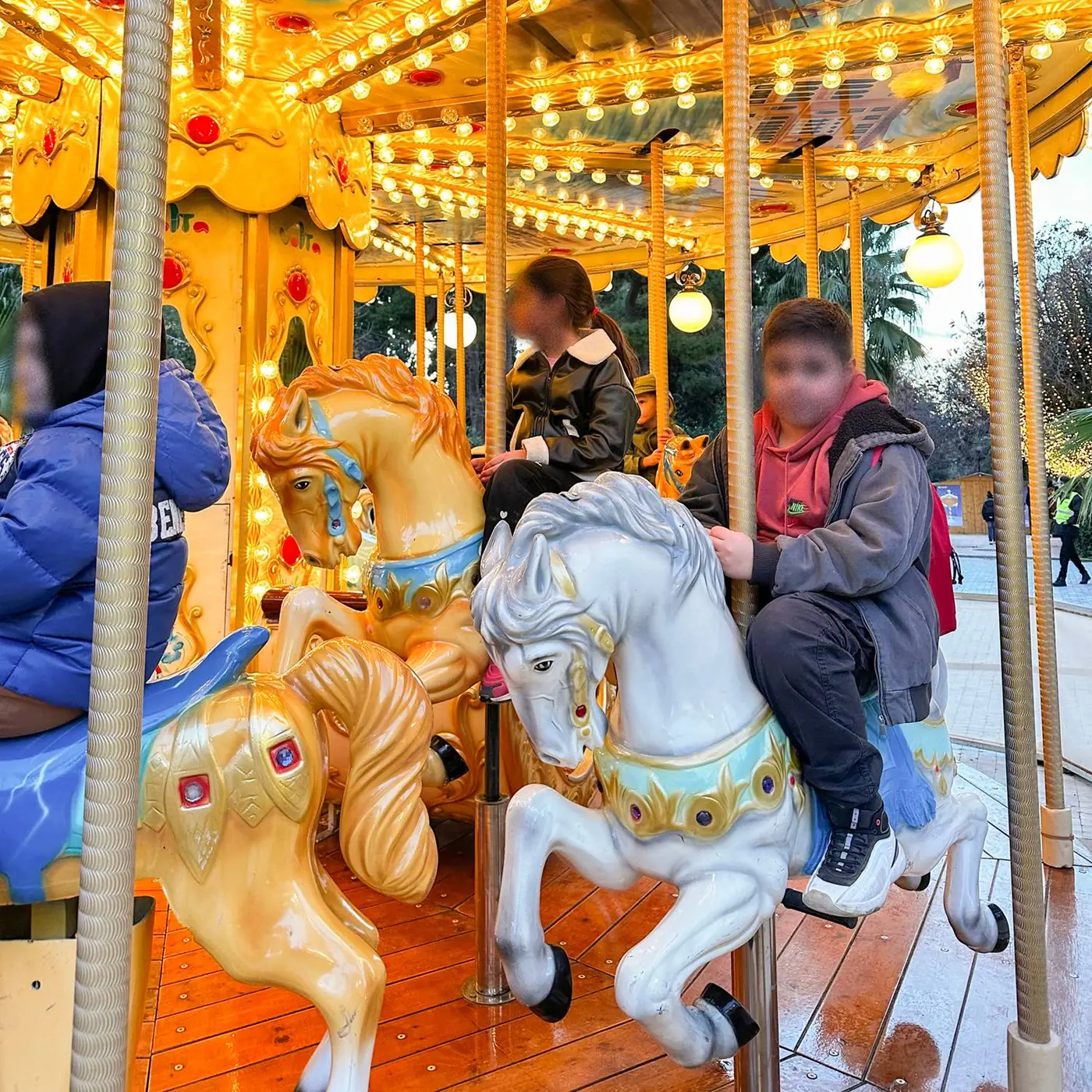 Kinderen op witte en gouden paardjes van een verlichte draaimolen in Pedion tou Areos, met vervaagde gezichten