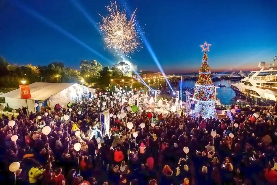 Menigte met witte ballonnen bij het ontsteken van de boom in Marina Flisvos, met vuurwerk in de lucht en jachten op het water