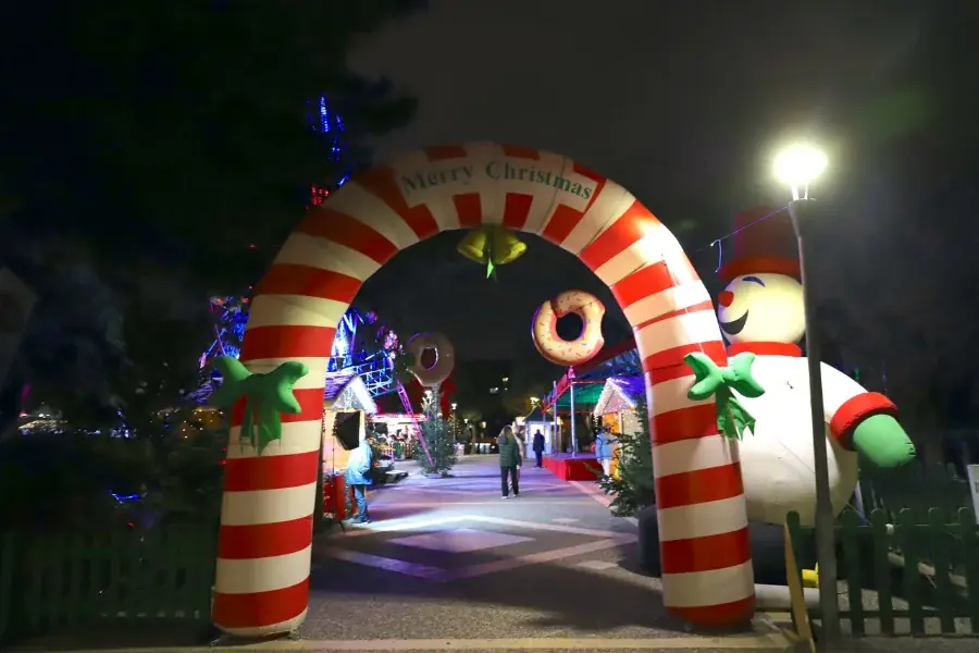 Opblaasbare boog in de vorm van een zuurstok met de tekst Merry Christmas en een opblaasbare sneeuwpop bij de ingang van het Kerstmanpark bij nacht