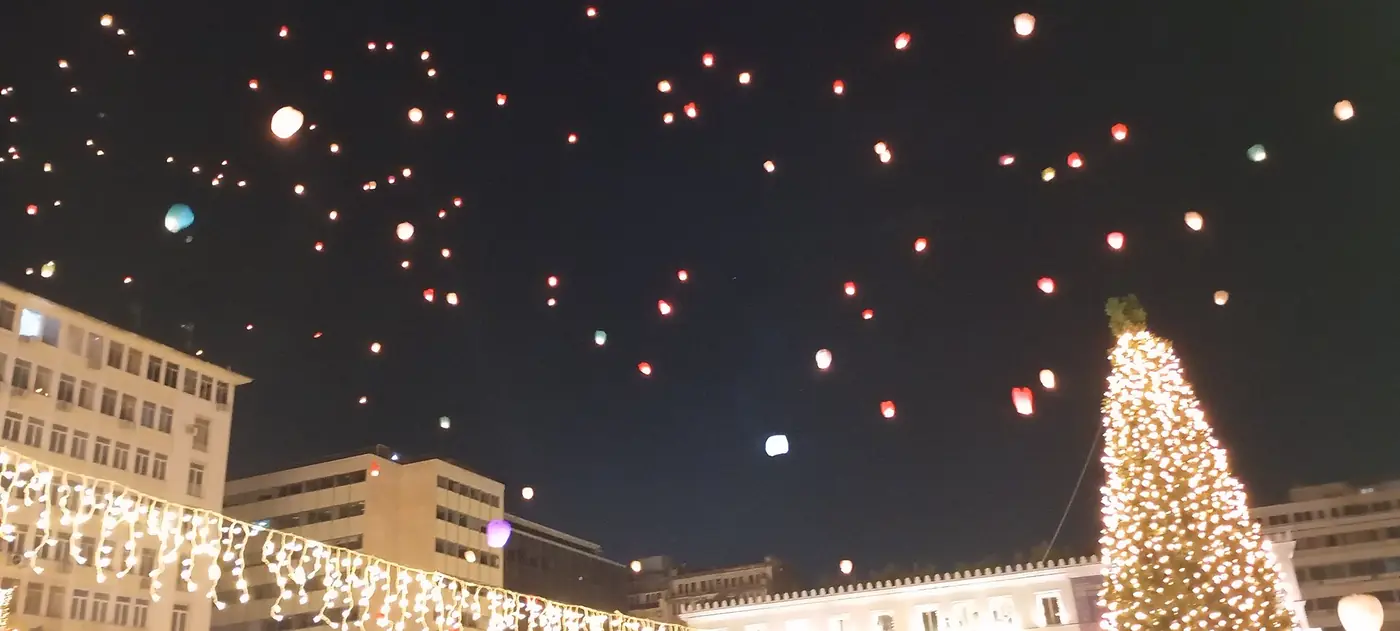 Tientallen lantaarns in de nachtlucht boven het Kotziaplein, met een verlichte spar en gebouwen op de achtergrond