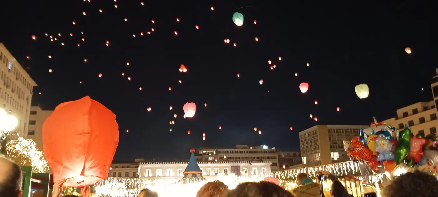 Lantaarns in de lucht met een rode lantaarn links en kinderballonnen eronder, op de markt