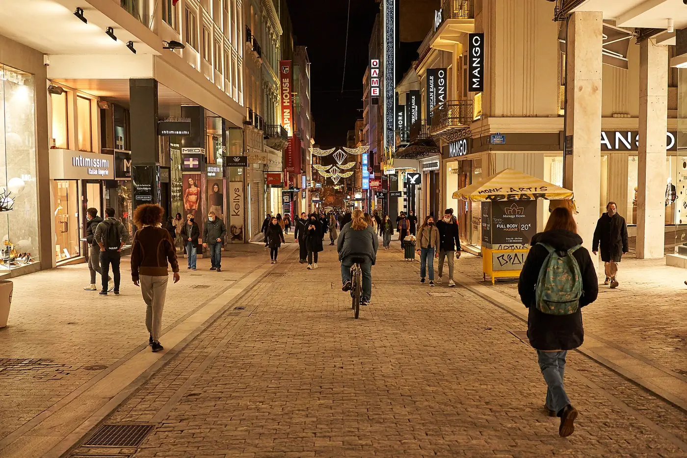 De voetgangersstraat Ermou ’s avonds met verlichte etalages en decoratieve lichten boven de voorbijgangers
