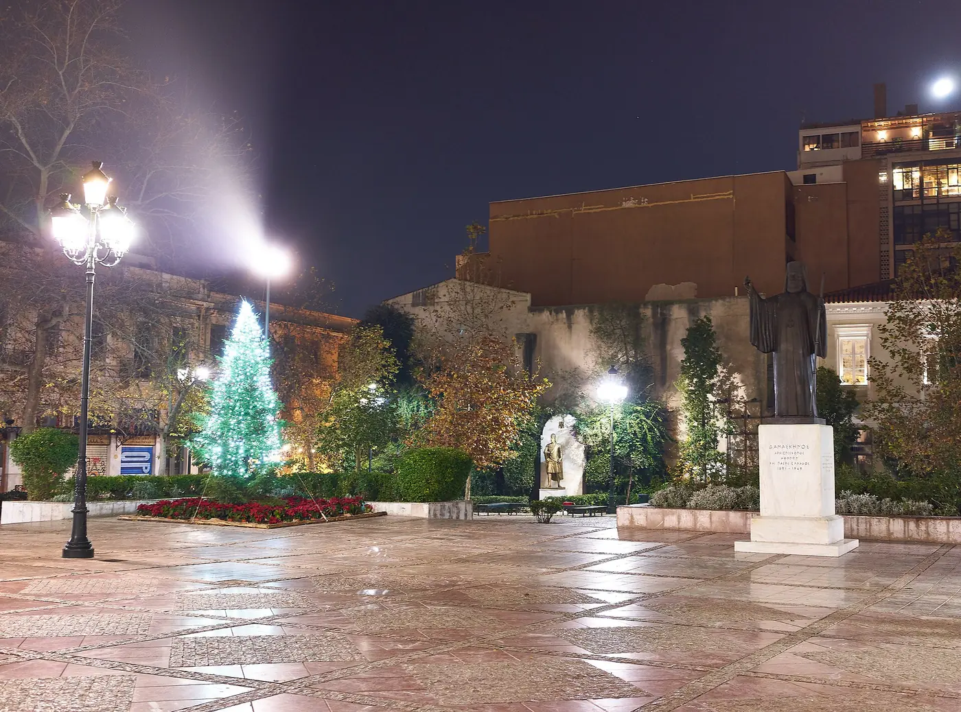 Kerstversiering op het Mitropoleosplein bij nacht, met een verlichte groene spar en beelden