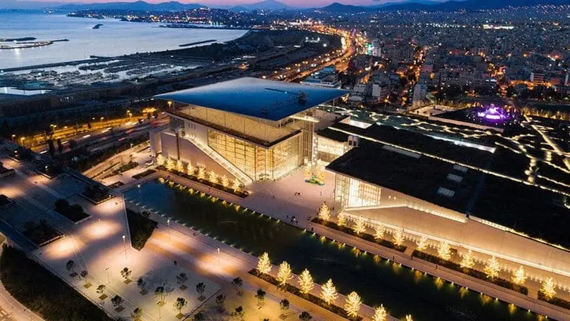 Het SNFCC van bovenaf in de schemering, met de verlichte bomen langs het Kanaal, het park en de jachthaven van Faliro op de achtergrond
