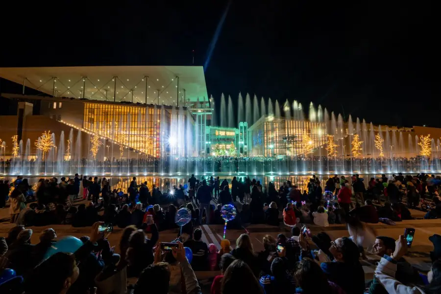 Menigte kijkt naar de fonteinen van het Kanaal die verlicht water spuiten voor het SNFCC-gebouw bij nacht