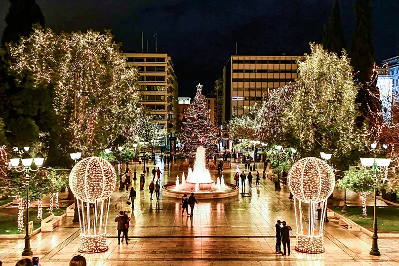 Het Syntagmaplein bij nacht van bovenaf, met verlichte bomen, de fontein, twee lichtgevende ballonnen en de kerstboom op de achtergrond