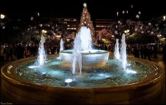 De fontein op het Syntagmaplein verlicht bij nacht, met de kerstboom en de verlichte bomen erachter