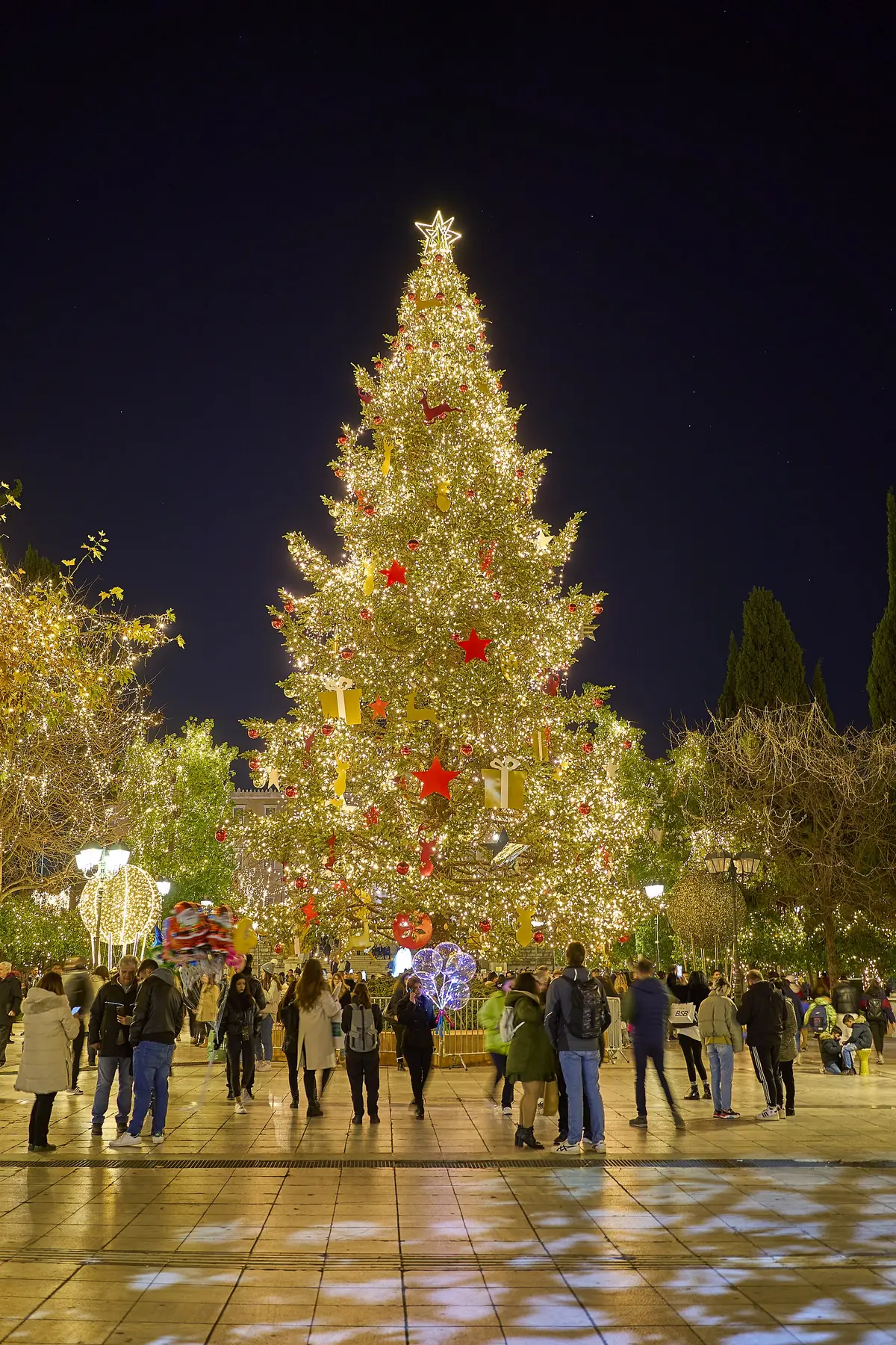 De boom van Syntagma met gouden lampjes en rode ballen, met voorbijgangers ervoor