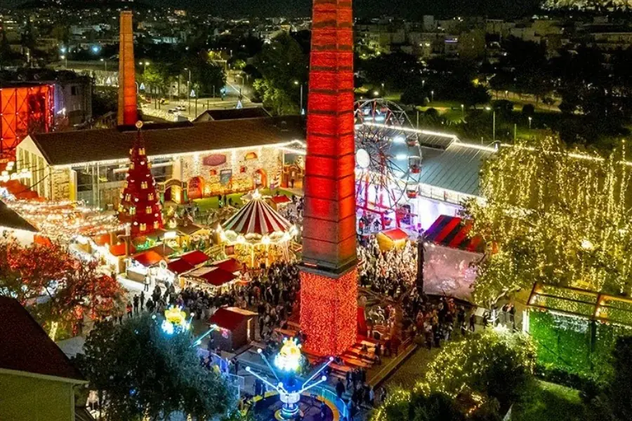 Technopolis van bovenaf bij nacht, met een schoorsteen in rode lichten, reuzenrad, draaimolen, rode boom en drukte tussen de kraampjes